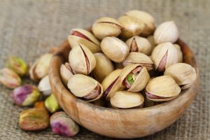 Pistachio nuts with and without shell in wooden bowl, close up